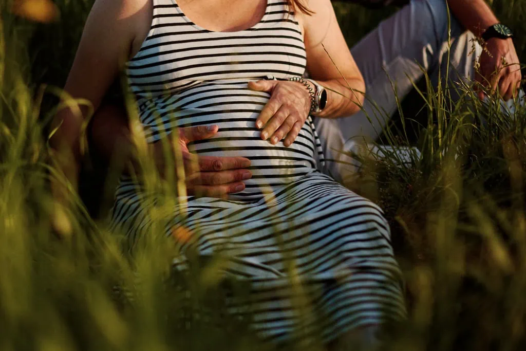 Femme enceinte assise dans l'herbe, main sur ventre.