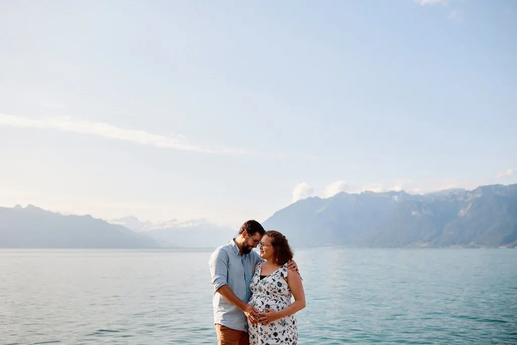 Couple souriant devant un lac et des montagnes.