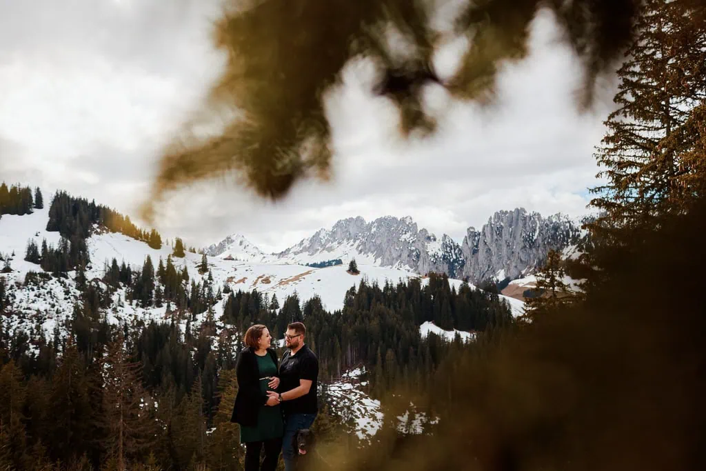Couple dans montagnes enneigées avec sapins.
