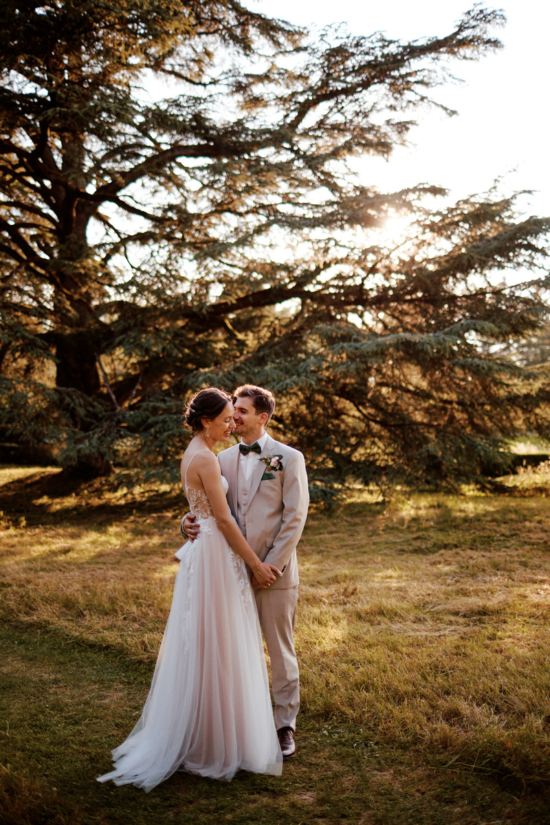 Mariés devant grand arbre au coucher du soleil.