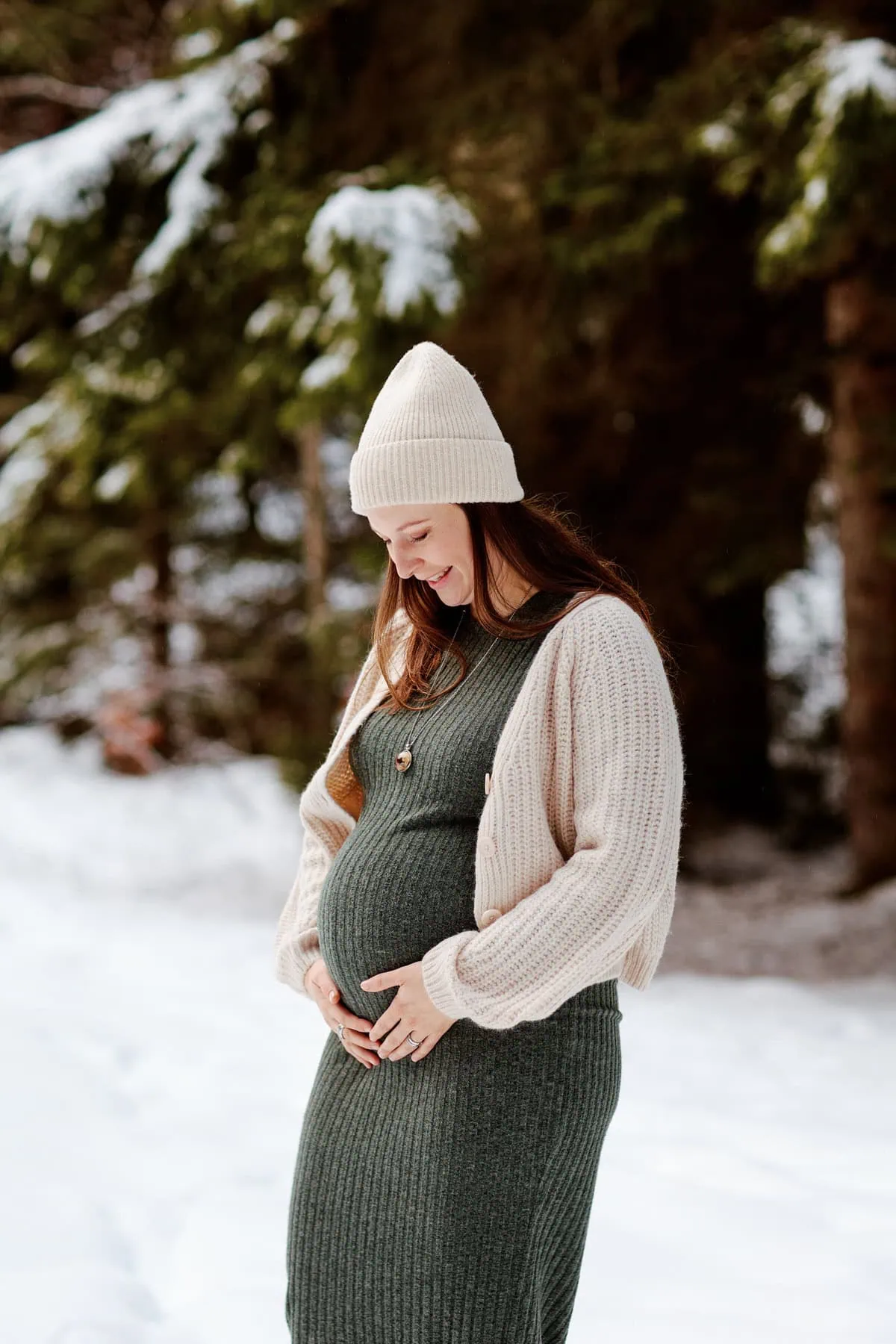 Femme enceinte souriante en forêt enneigée.