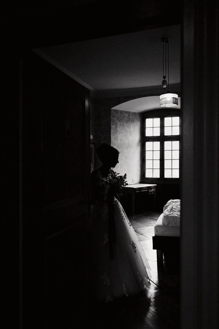 Mariée dans une pièce sombre près de fenêtre.