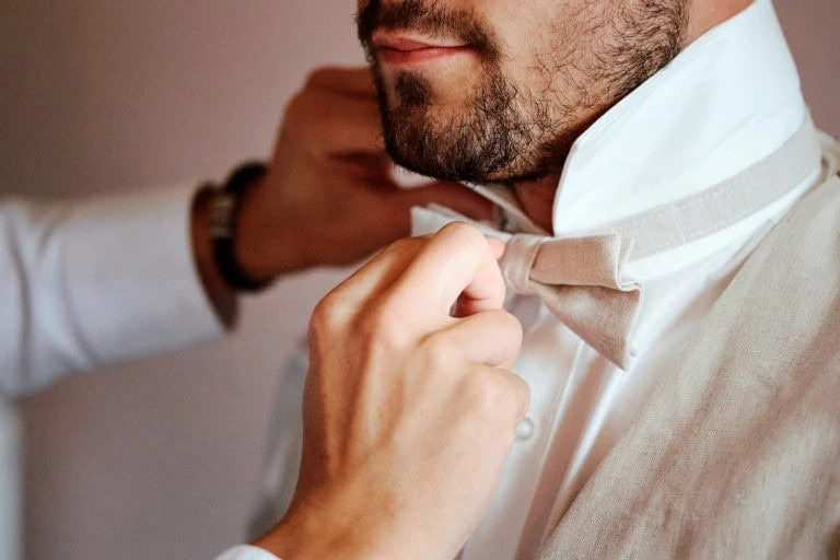 Homme ajustant un nœud papillon beige avec soin.