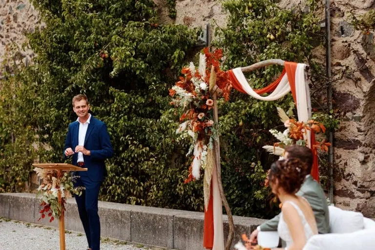 Homme en costume bleu parle lors d'une cérémonie extérieure.