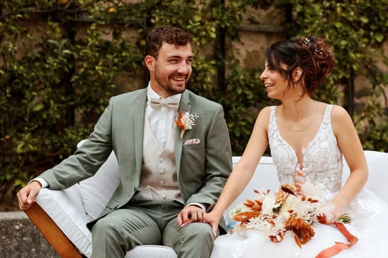 Couple marié souriant, assis avec bouquet.