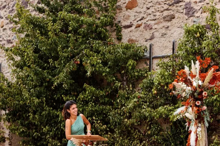 Femme souriante devant mur fleuri.
