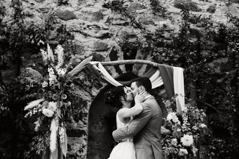 Couple s'embrassant devant arche fleurie.