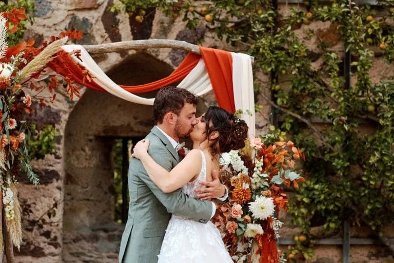 Couple marié s'embrassant sous une arche florale.