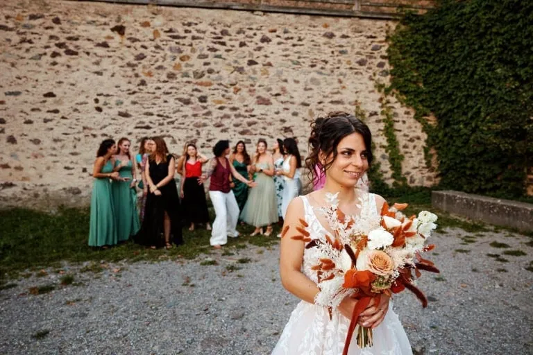 Mariée souriante avec bouquet, femmes en arrière-plan.