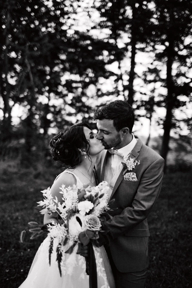 Mariés s'embrassant devant arbres.