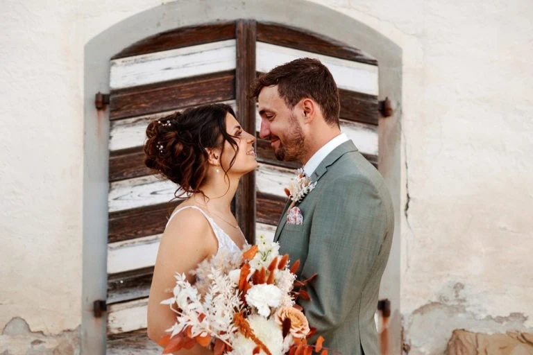 Couple marié heureux avec bouquet devant porte bois.
