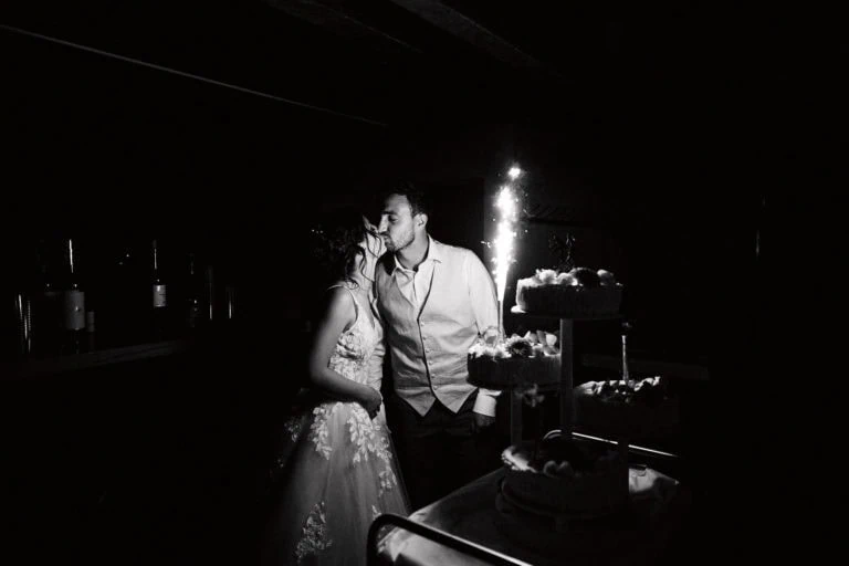 Couple s'embrassant devant gâteau de mariage.