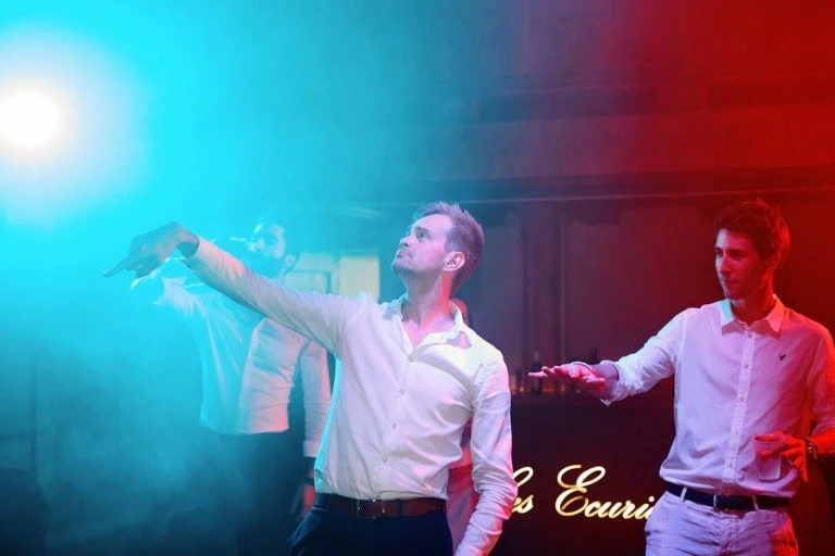 Trois hommes dansent sous lumières colorées.