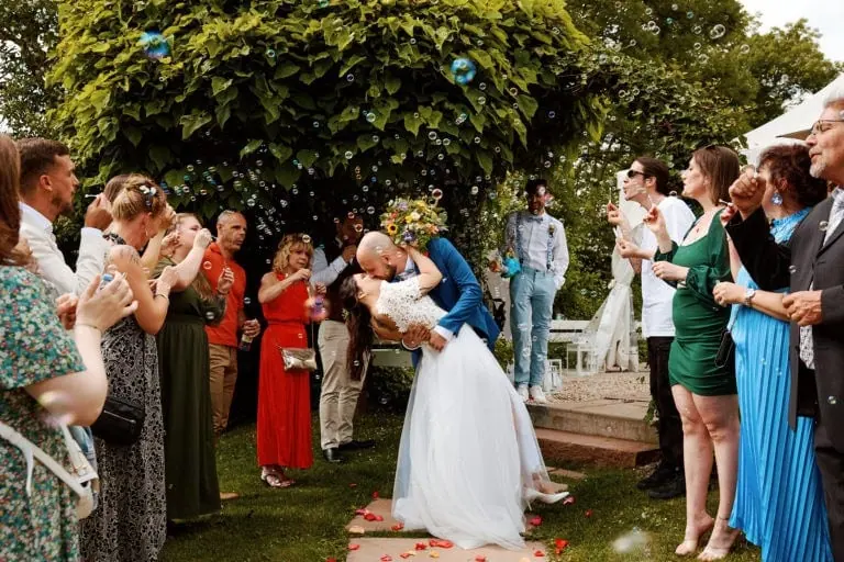 Mariage, couple s'embrassant entouré d'invités et de bulles.