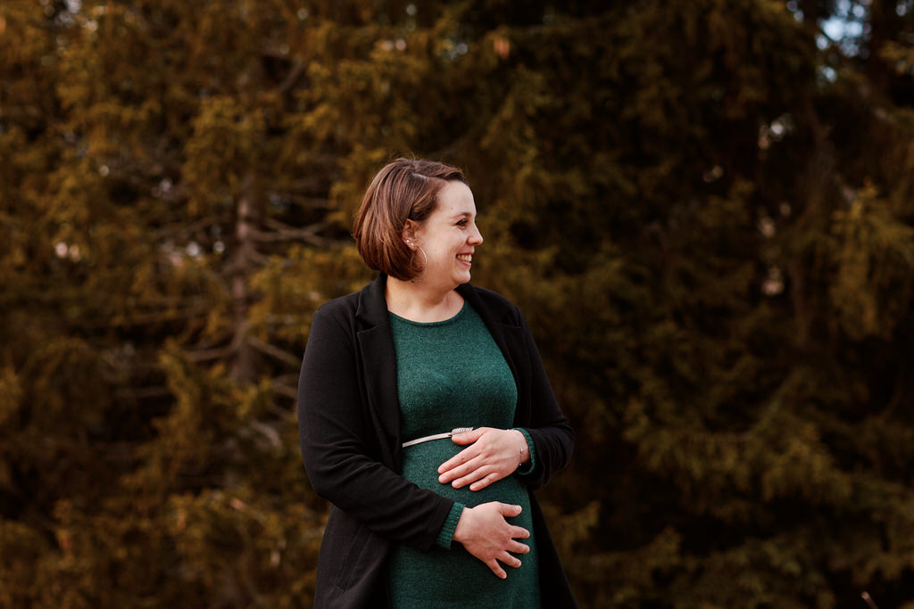 Femme souriante en robe verte devant arbres.