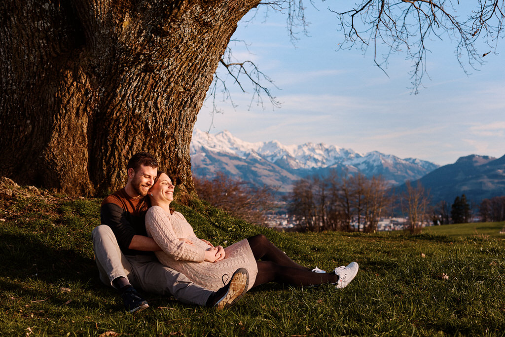 Couple assis sous un arbre avec montagnes enneigées.