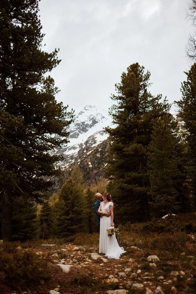 Couple marié embrassant en montagne enneigée.