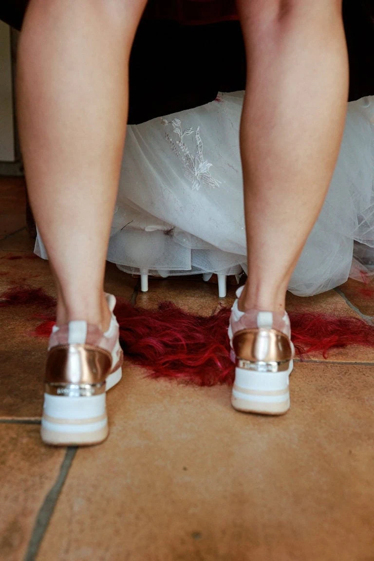 Personne en baskets dorées, jupe blanche, sol rouge.