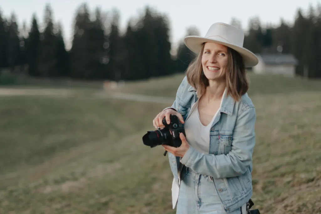 Femme souriante tenant un appareil photo dans un champ.