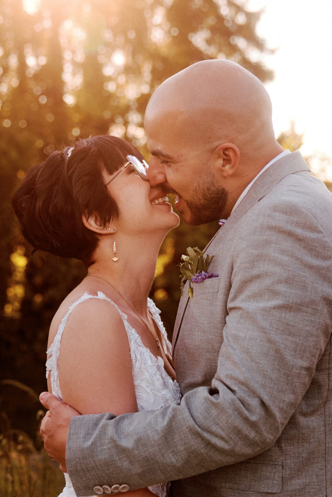 Séance couple au coucher du soleil, les mariés rient et s’embrassent en lumière dorée.