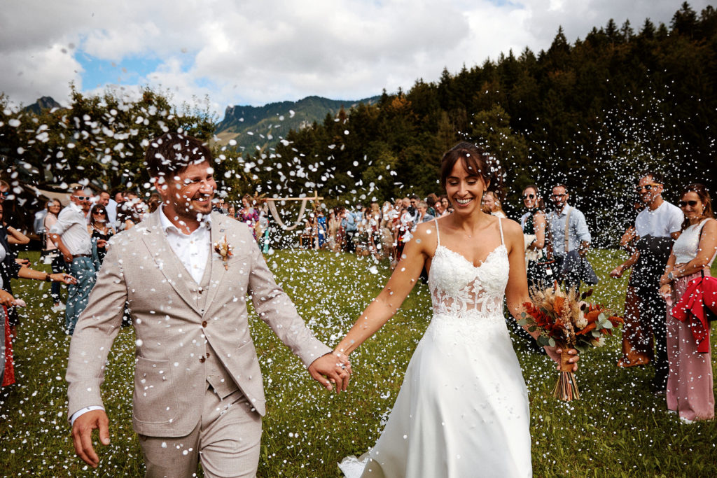 Sortie de cérémonie en extérieur, les mariés marchent main dans la main sous une pluie de confettis.