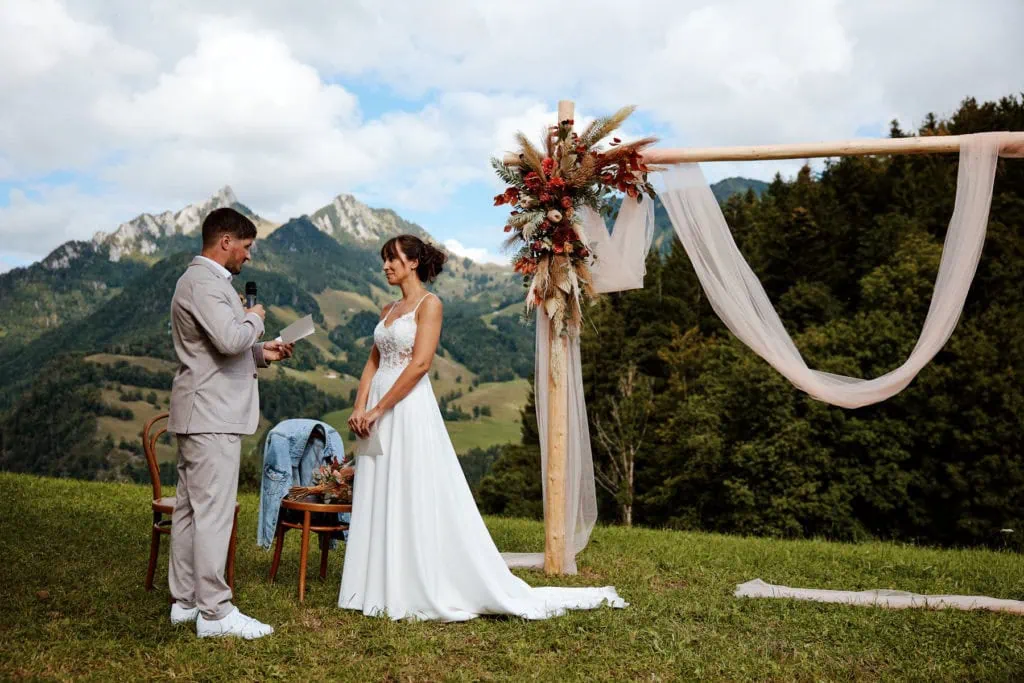 Cérémonie de mariage en plein air en montagne, échange de vœux devant une arche fleurie