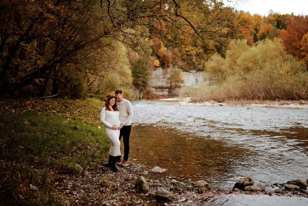 Couple de futurs parents heureux en forêt, près d'une rivière.
