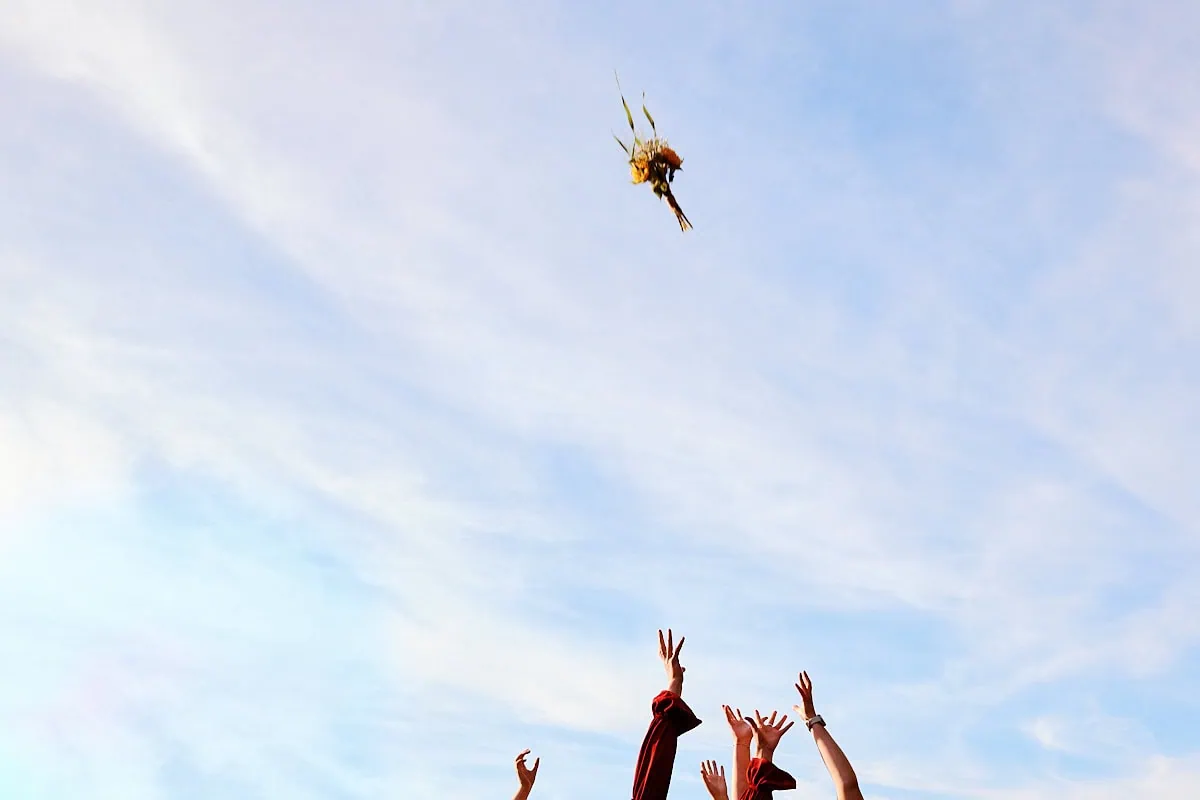 Mains levées attrapant un bouquet lancé dans le ciel.