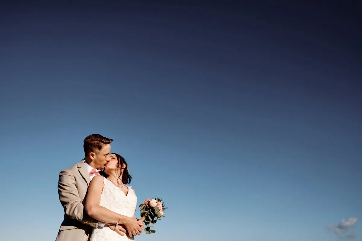 Couple de mariés s’embrassant sous un ciel bleu