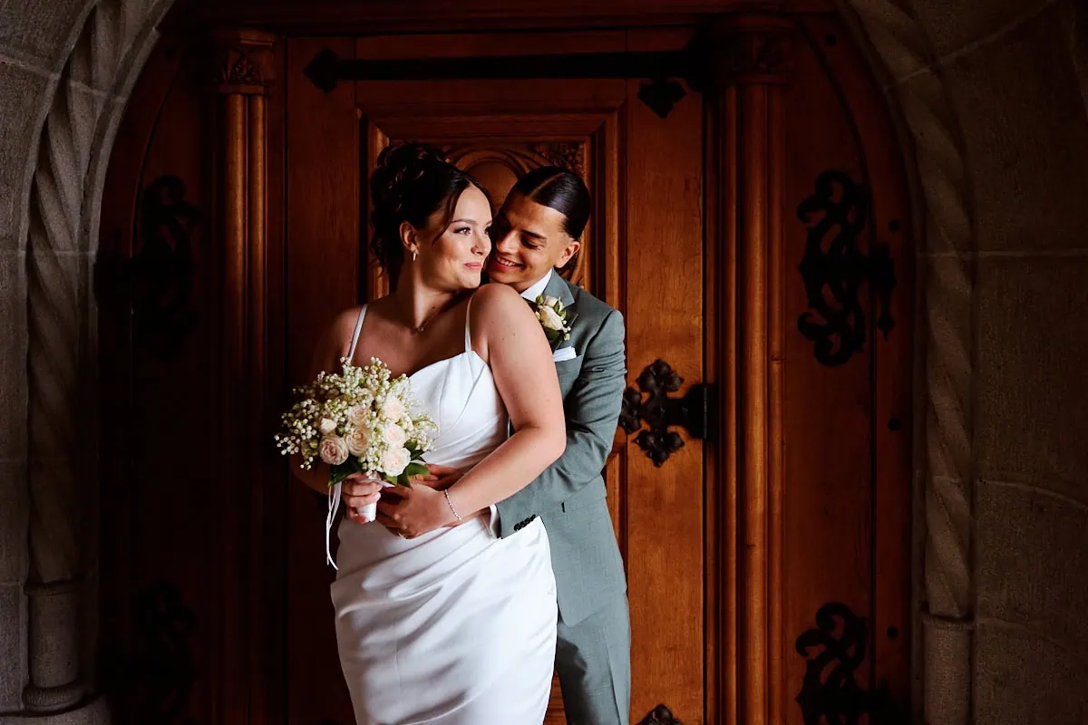 Couple de mariés s’enlaçant devant une porte en bois.