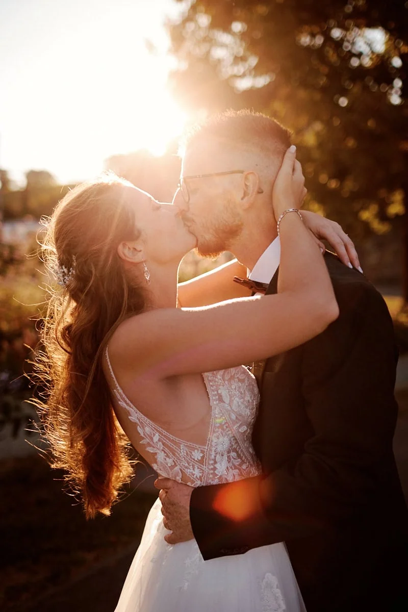 Couple marié s’embrassant lors d’un moment romantique en extérieur au coucher du soleil.