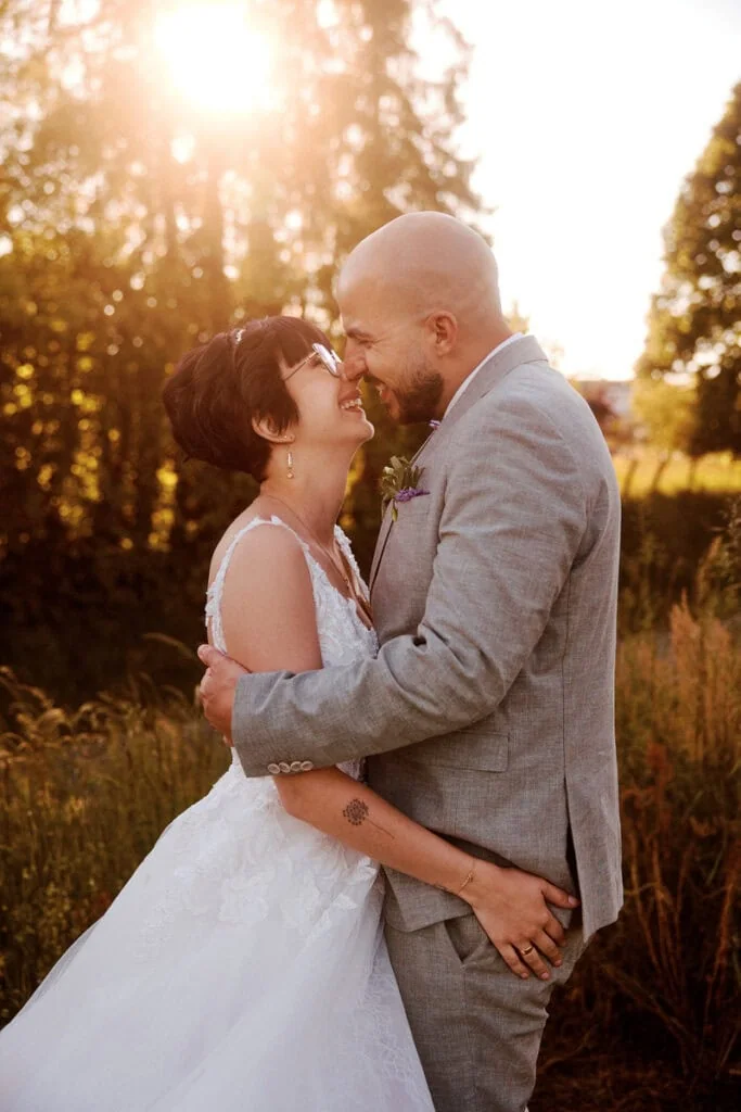 Couple de mariés souriants lors d'une séance photo en extérieur au coucher du soleil.